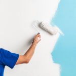 Back view of painter painting a wall with paint roller, with copy space